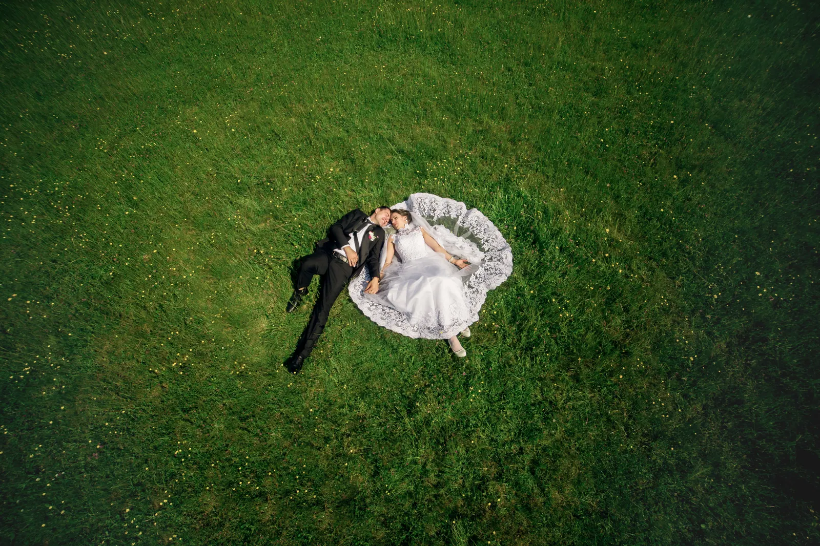Plano cenital con dron de una pareja de novios tumbada sobre el césped el día de su boda